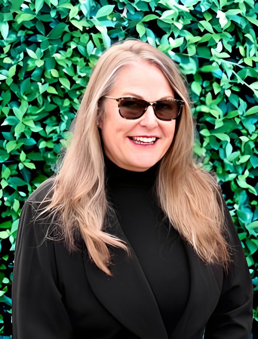 Woman smiling in front of leafy background.