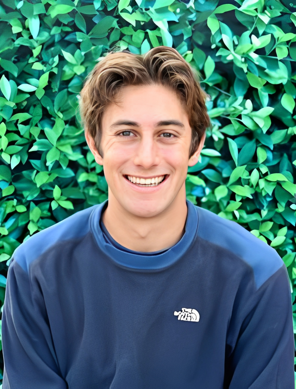 Smiling person in front of green foliage.